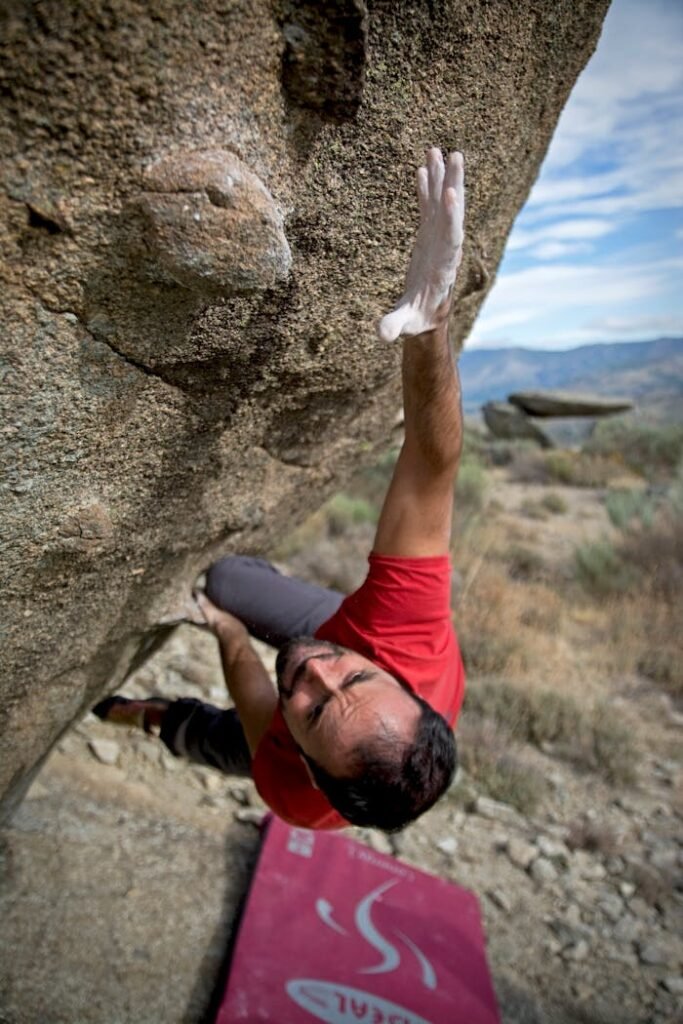 Man in red shirt bouldering on a steep rock face, showcasing strength and determination.